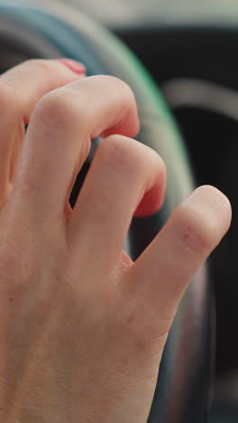 female hands with red manicure hold steering wheel of car. woman taps fingers nervously standing in traffic jam on blurred background closeup