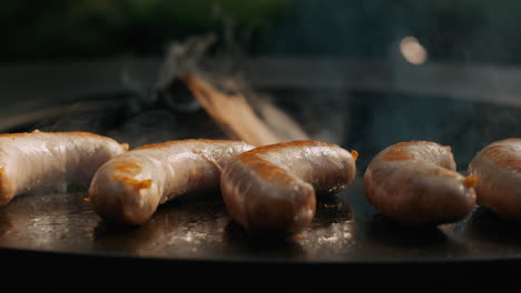 Salchichas-Jugosas-Preparándose-En-Una-Parrilla-Redonda-Afuera.-Salchichas-Dorándose-A-La-Parrilla