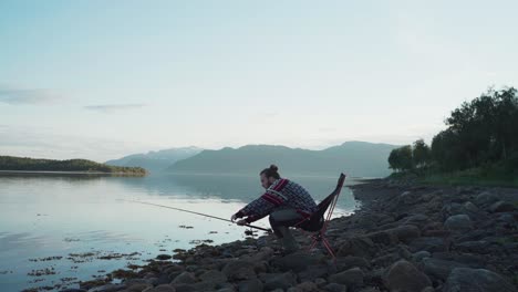 Hombre-Pescando-Sentado-Junto-A-La-Orilla-Rocosa-Del-Lago-Cerca-De-Vangsvika,-Noruega