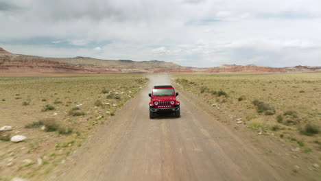 jeep wrangler rojo conduciendo por un polvoriento camino de tierra del desierto en utah