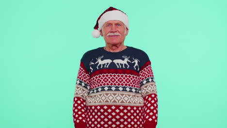 Grandfather-man-in-Christmas-sweater-with-deers-waves-hand-palm-in-hello-gesture-welcomes-someone