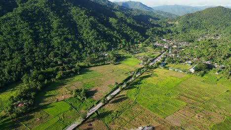 Vibrant flyover shot of provincial town road amid lush greenery, hills and rice fields at Lictin, San Andres, Catanduanes, Philippines.