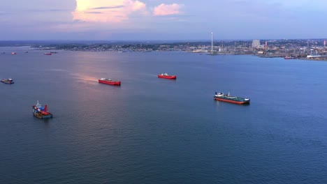 panning aerial view of oil tankers and pertamina oil refinery in the background during sunset - port of balikpapan - east kalimantan, indonesia