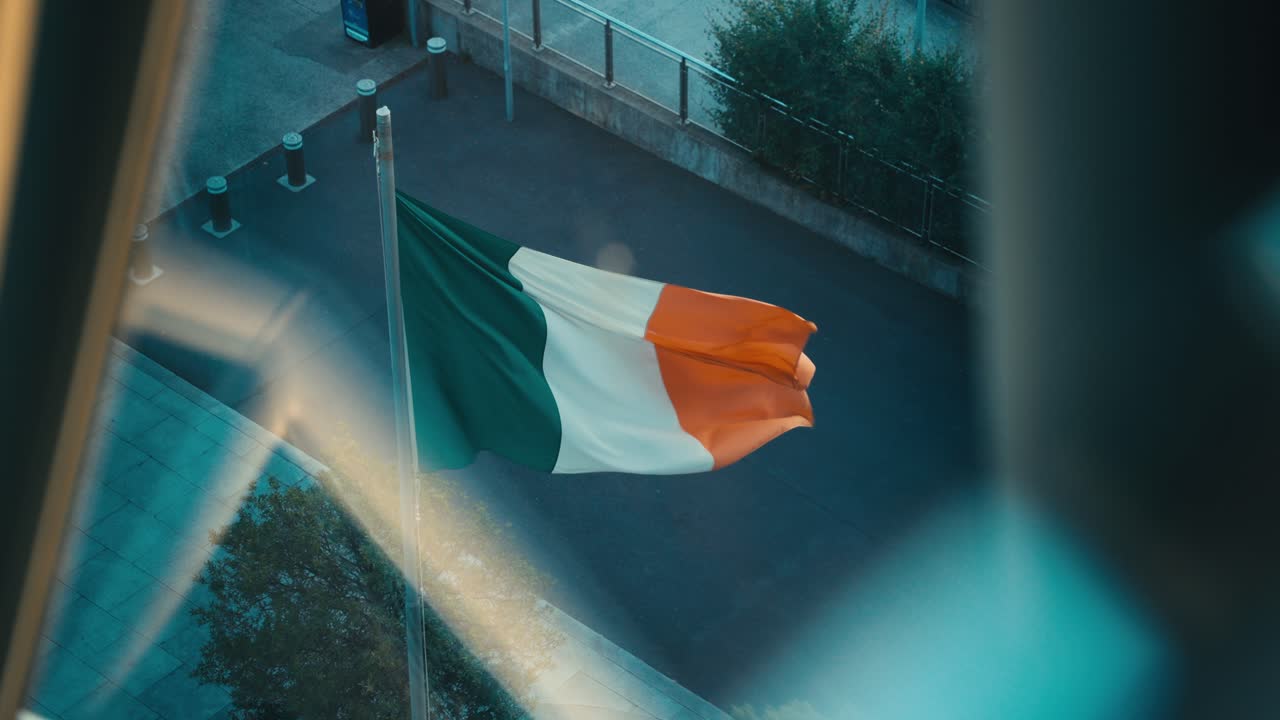 An Irish flag flies in slow motion with a glass reflection. Flag of Ireland.