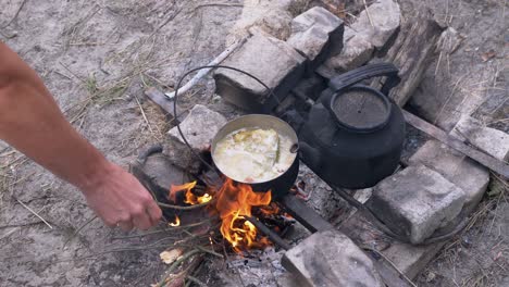 male preparing food in a saucepan on a bonfire in woods outdoors. 4k. close up