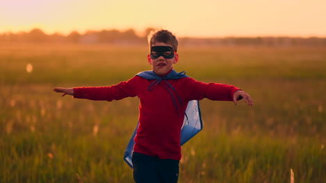 Junge-Im-Superheldenkostüm-Und-Mit-Maske-Rennt-Bei-Sonnenuntergang-Träumend-Und-Phantasievoll-über-Das-Feld.