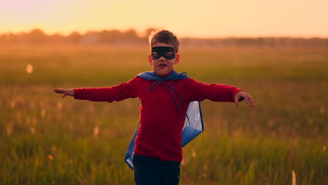 un niño con disfraz de superhéroe y máscara corriendo por el campo al atardecer soñando y fantaseando.