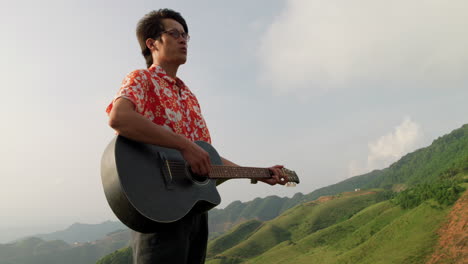 asian male playing acoustic guitar outdoors in nature,medium shot