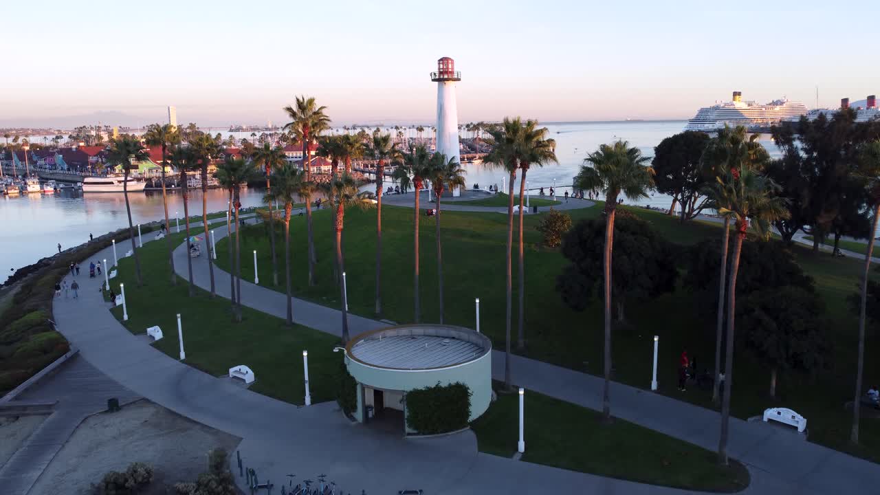 Establishing shot of Long Beach's Lions Lighthouse. Sunset showing the harbor marina, waterfront walkways, docked cruise ship and calm waters of Queensway Bay at the mouth of the LA River SoCal