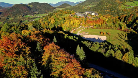 Aerial-shots-of-deep-forest-autumn-colors-blanket-the-landscape-near-Attersee,-Austria,-with-a-clear-view-of-the-surrounding-hills-and-a-building-complex
