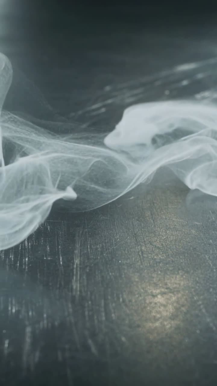 Vertical video: Drifting white smoke ribbon moving from off frame, curling on wood tabletop sheen