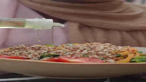 mujer vertiendo aceite en una ensalada de quinoa