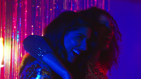 two women friends having fun in nightclub or bar dancing against sparkling tinsel curtain in background