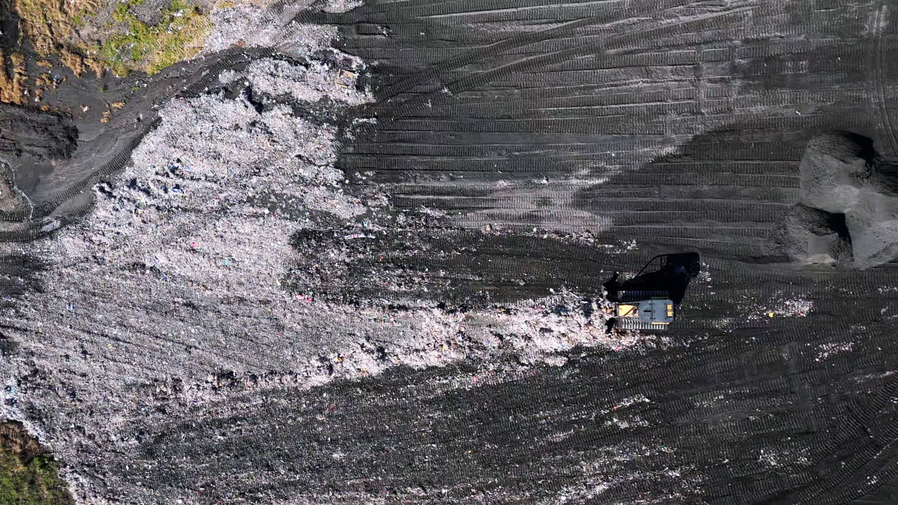Top down static aerial footage of a bulldozer pushing trash around in a landfill
