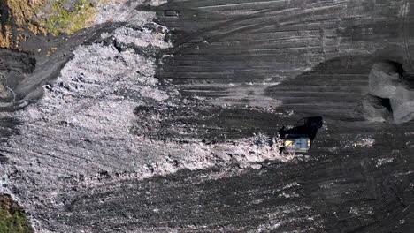 imágenes aéreas estáticas de arriba hacia abajo de una excavadora empujando basura alrededor de un vertedero