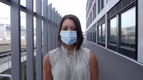 young woman standing between metal grille with a hygienic respirator mask over her nose and mouth - listen to music