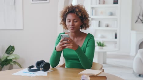 young african american woman with phone looking dreamily to side sits at table