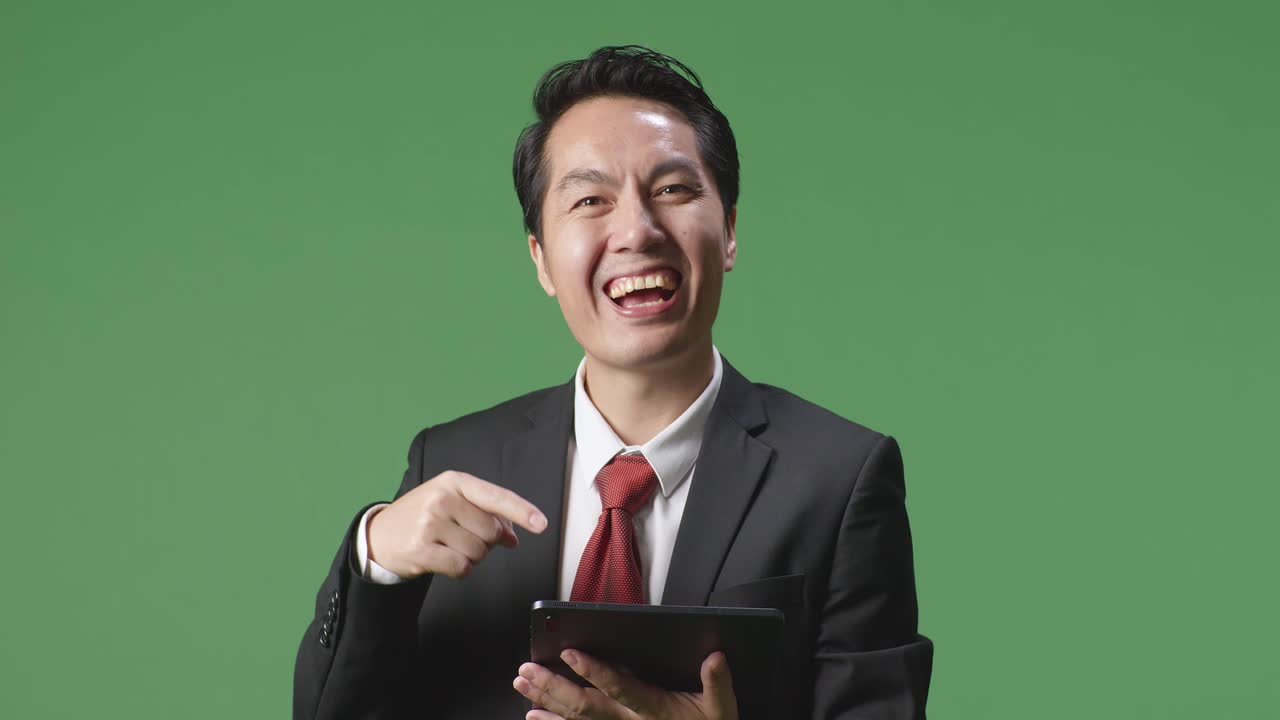 스튜디오에서 녹색 화면 배경에 태블릿을 사용하고 가리키는 동안 미소 짓는 아시아 사업가