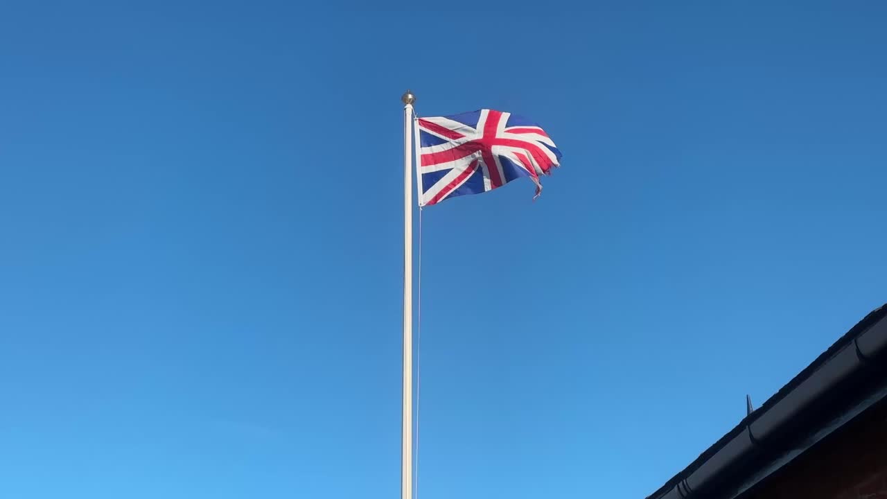 Det britiske flag Union Jack vajer i vinden mod en klar blå himmel. Nationalt symbol for patriotisme i Storbritannien.