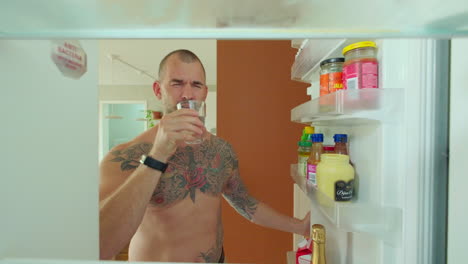 man drinking water in refrigerator in the kitchen - close up