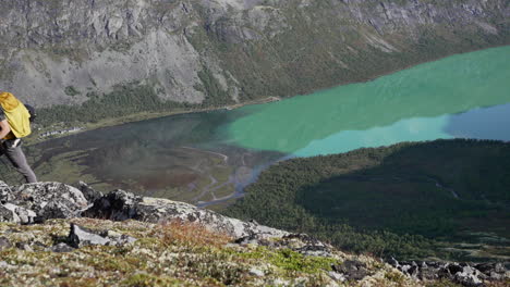 Diagonal-top-down-view-of-male-hiking-hill-side-with-green-lake-in-backgroud-during-early-sunny-autumn-morning