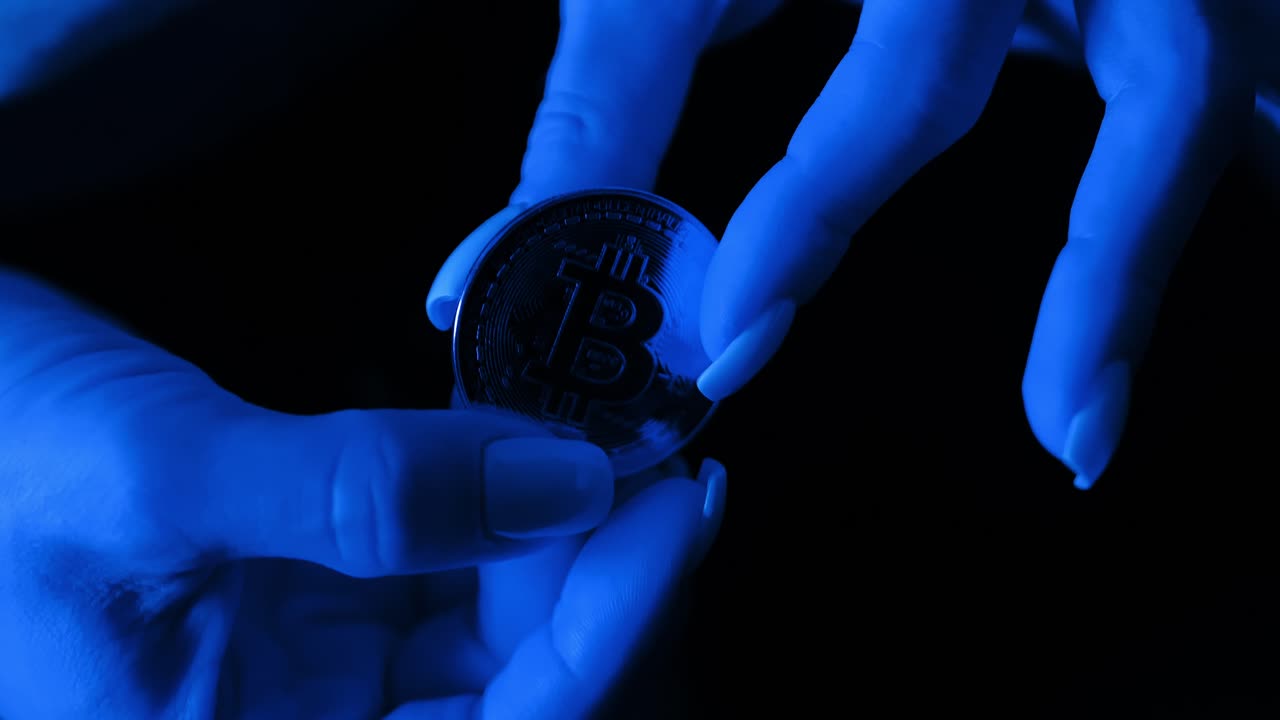 Hands holding Bitcoin coin in moody deep blue glow, blockchain, fintech, wealth