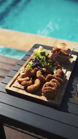 primer plano de bocadillos fritos servidos en una tabla de madera por una piscina en un complejo turístico