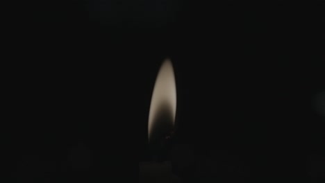 a closeup shot of a glowing candle flame slowly swaying, surrounded by darkness