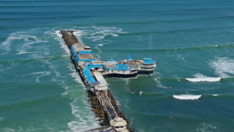 la rosa nautica along pier cutting through waves, ocean surf hitting both sides, slow motion, lima peru