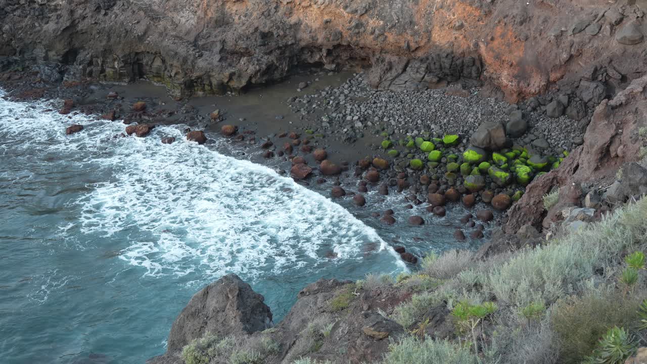 Ondas do mar avançando em direção à costa rochosa, vistas de um penhasco, em câmera lenta estática manual.