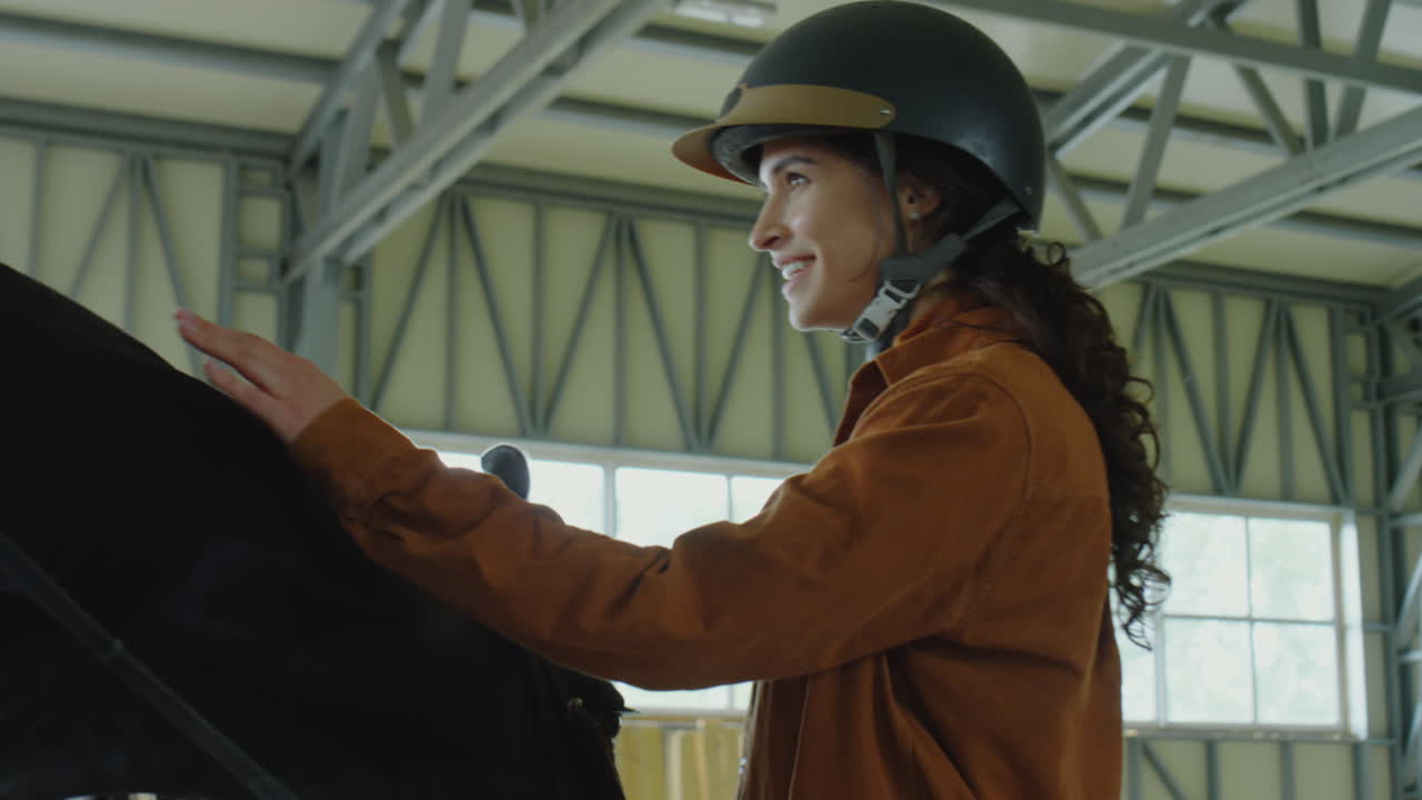 A woman in a riding helmet bonding with a horse in a stable
