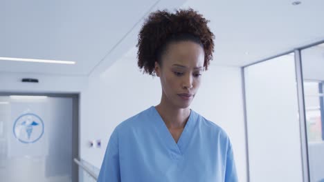 Happy-mixed-race-female-medical-staff-standing-in-hospital-corridor-looking-at-documents