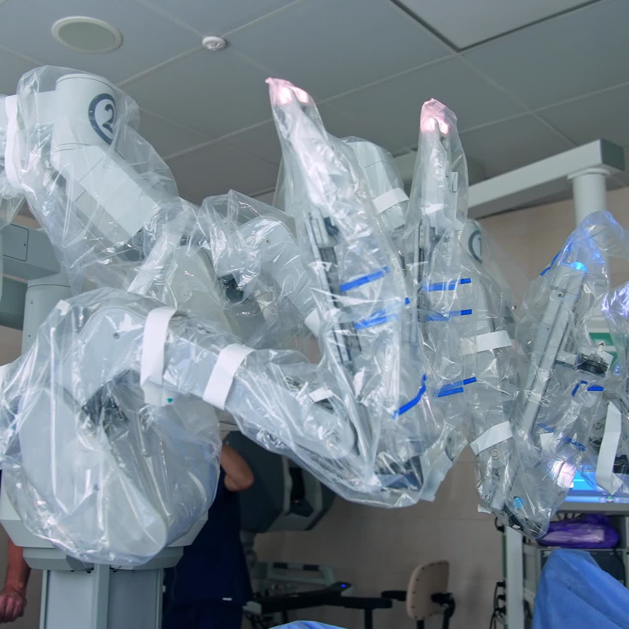 Medical workers standing behind the modern surgery equipment. Da Vinci robot coated with plastic for sterility at operation