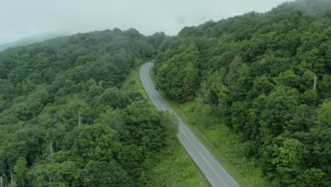 Statische-Antenne-Eines-Autos,-Das-Auf-Einer-Nebligen-Bergwaldstraße-Um-Die-Kurve-Fährt,-4k