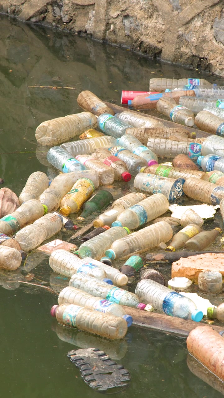 Inquadratura media statica di bottiglie di plastica scartate e rifiuti che galleggiano in un canale sporco.