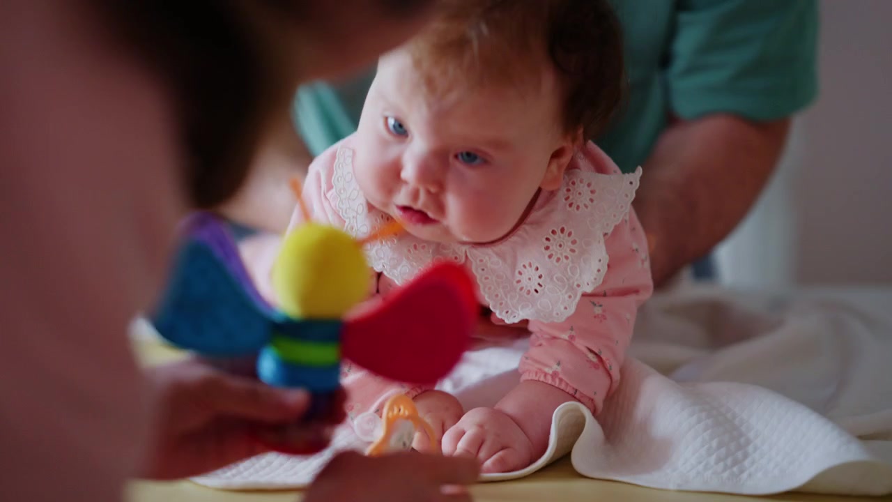 Healthcare professional wearing a medical mask gently supporting a baby during a pediatric care session with a colorful toy nearby