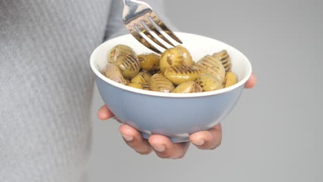 una persona sosteniendo un cuenco de aceitunas verdes con un tenedor