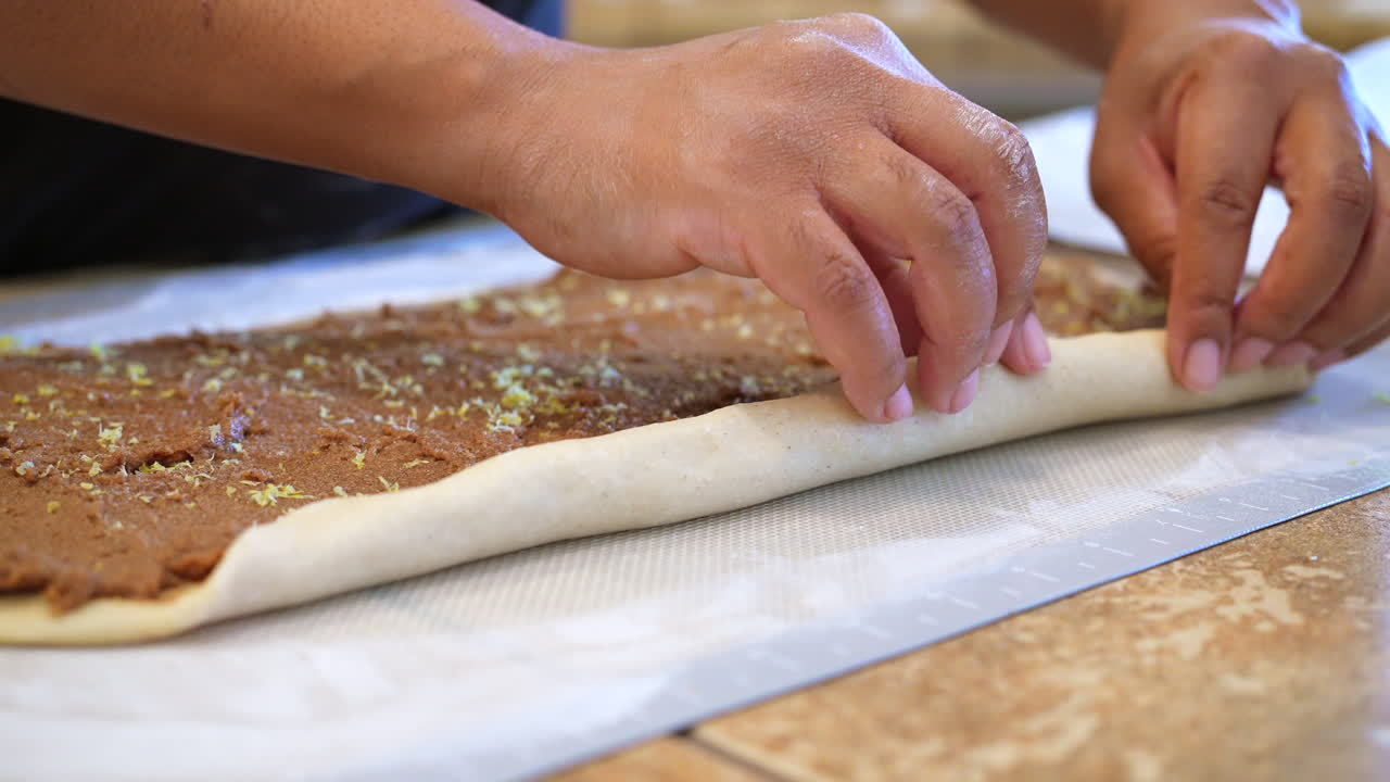 enrollando masa recién amasada y relleno de canela azucarada en un pan para cortar y hornear - vista lateral