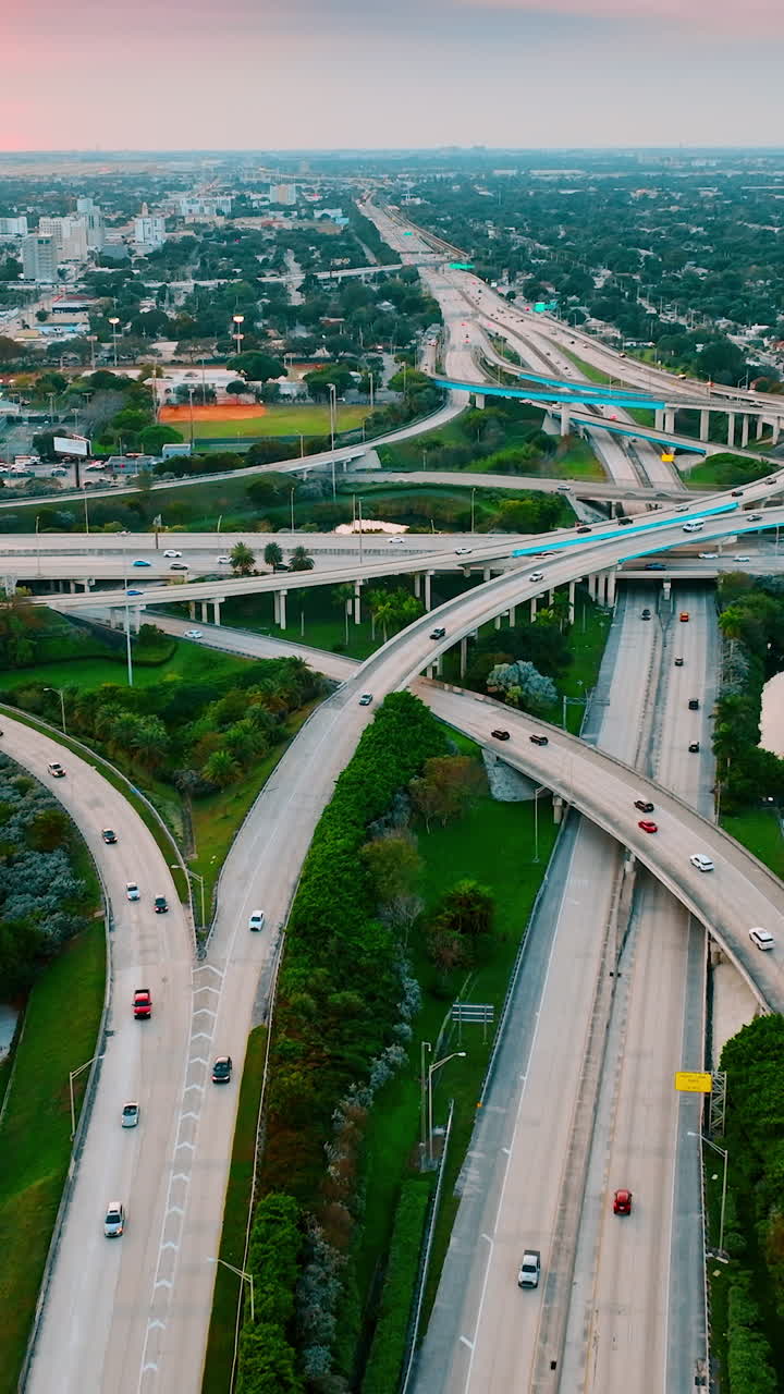 Splendid view of Miami district with large road interchange. Multiple cars run by the highways and freeways in green area of the city. Aerial perspective. Vertical video