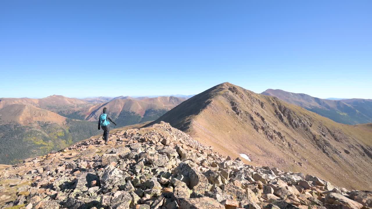 excursionista femenina caminando sola en una cordillera de montaña rocosa en un día sin nubes, estática