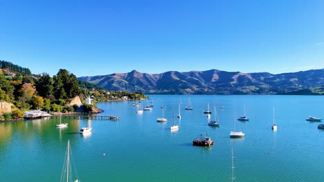 boats gently float in akaroa harbour under clear blue skies, surrounded by lush hills and calm waters