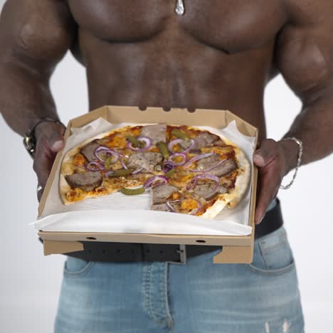 tasty pizza in hands of african man. black skinned guy with muscular body proposing delivered pizza in carton on studio background