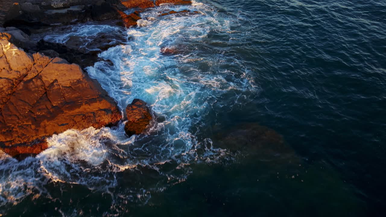Rocky coastline and waves crashing on shore, sunset in genoa, italy, aerial view