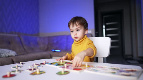 beautiful dark-haired baby boy in yellow sweater sitting at desk. smart little kid collecting puzzles.