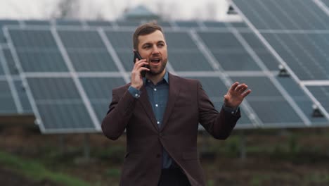 Un-Hombre-Sólido-Vestido-De-Negocios-Está-Hablando-Por-Teléfono-Con-El-Telón-De-Fondo-De-Los-Paneles-Solares