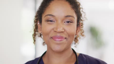 video portrait of happy biracial female doctor smiling in hospital corridor