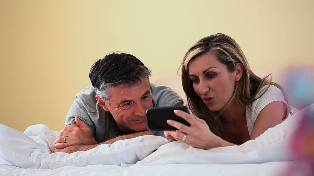 pareja sonriente mirando el teléfono inteligente tendido en la cama