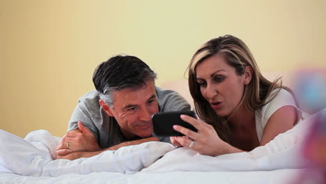 smiling couple looking at smartphone lying on bed