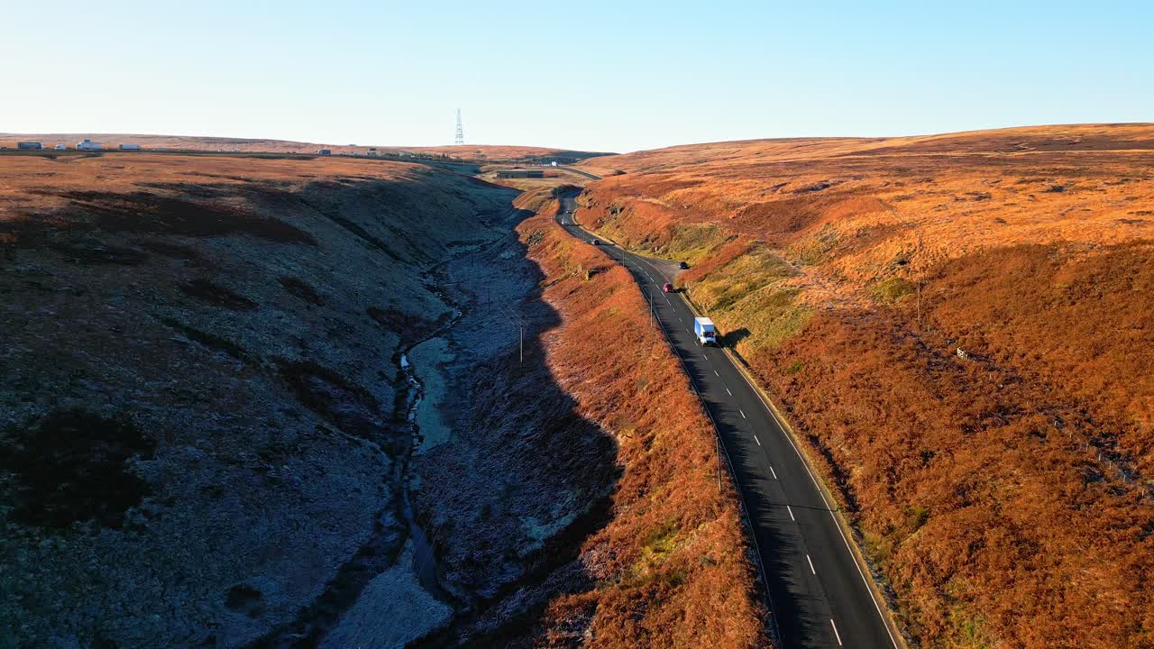 vista aérea de páramos en movimiento de una calle tranquila en el páramo de saddleworth, que muestra un paisaje salvaje con tráfico, embalse y páramos bordeados de nieve