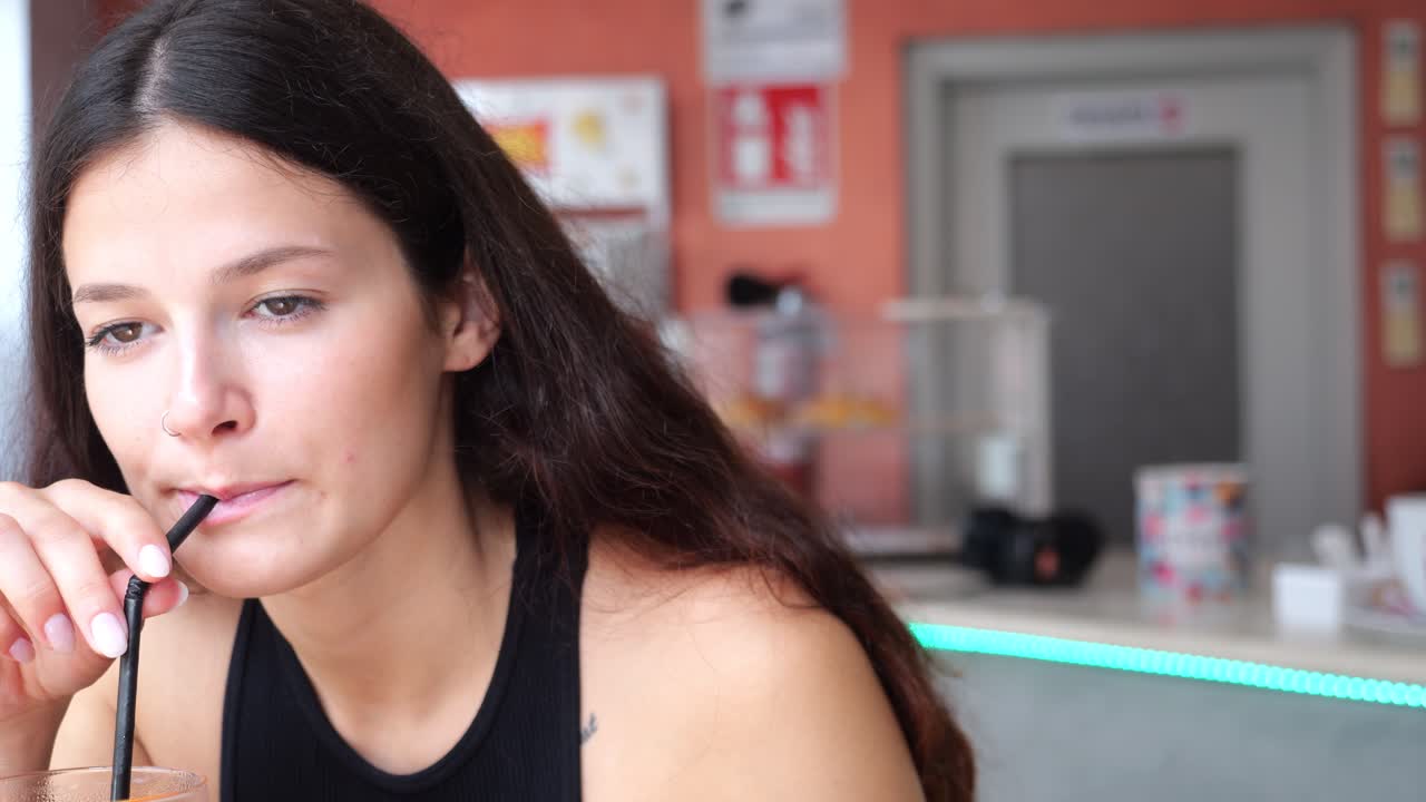 Close-up profile of woman actively chewing food with concentrated expression in a casual bar environment, followed by sipping from a beverage in a single continuous moment
